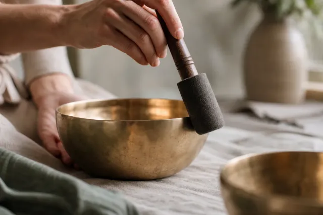 Hand schlägt eine Klangschale mit einem Filzschlägel sanft an
